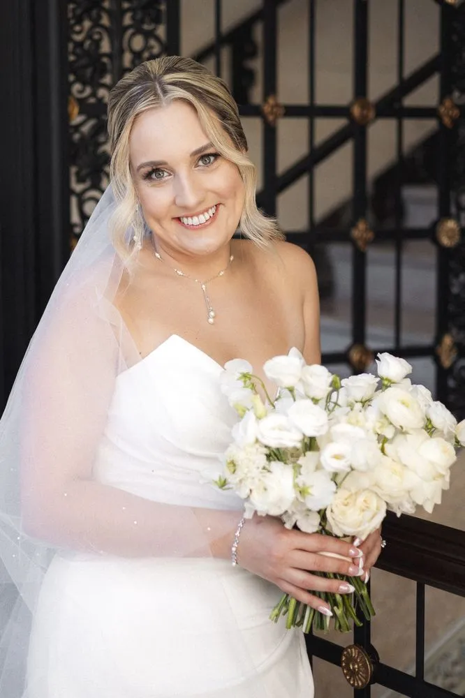 Bride with veil and necklace holding bouquet at iron gates