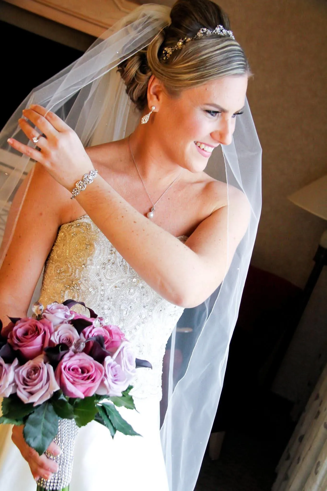 Bride with veil, tiara, and bracelet holding rose bouquet